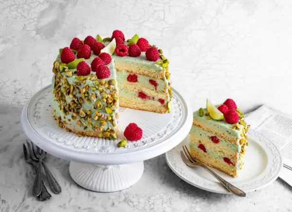 Pyszny tort pistacjowo malinowy, udekorowany świeżymi malinami i pistacjami, kusi swoim wyglądem i smakiem.
