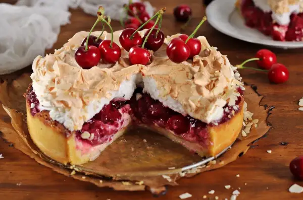 Pyszna tarta z czereśniami, udekorowana bezą i płatkami migdałów, kusi soczystym nadzieniem.