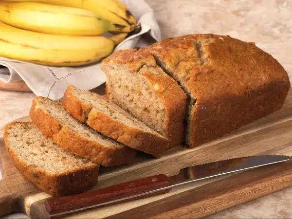 Pyszny chlebek bananowy bez cukru, pokrojony na kromki, leży na desce obok pęczka bananów.