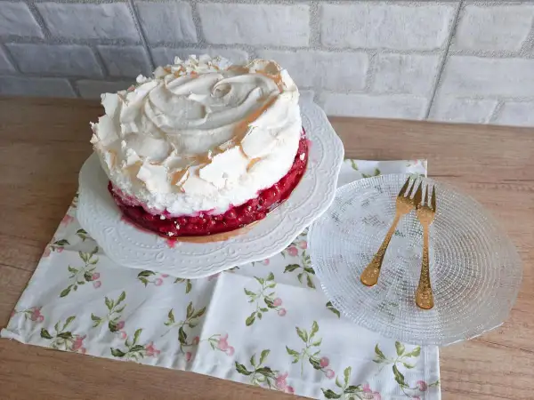 Pyszna tarta z porzeczkami, udekorowana puszystą bezą. Obok talerzyk z dwoma złotymi widelczykami.