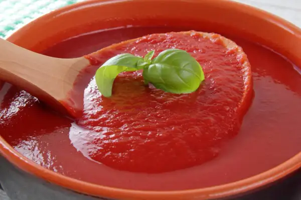Gęsty, czerwony ketchup z pomidorów, nabierany drewnianą łyżką, ozdobiony listkiem bazylii.